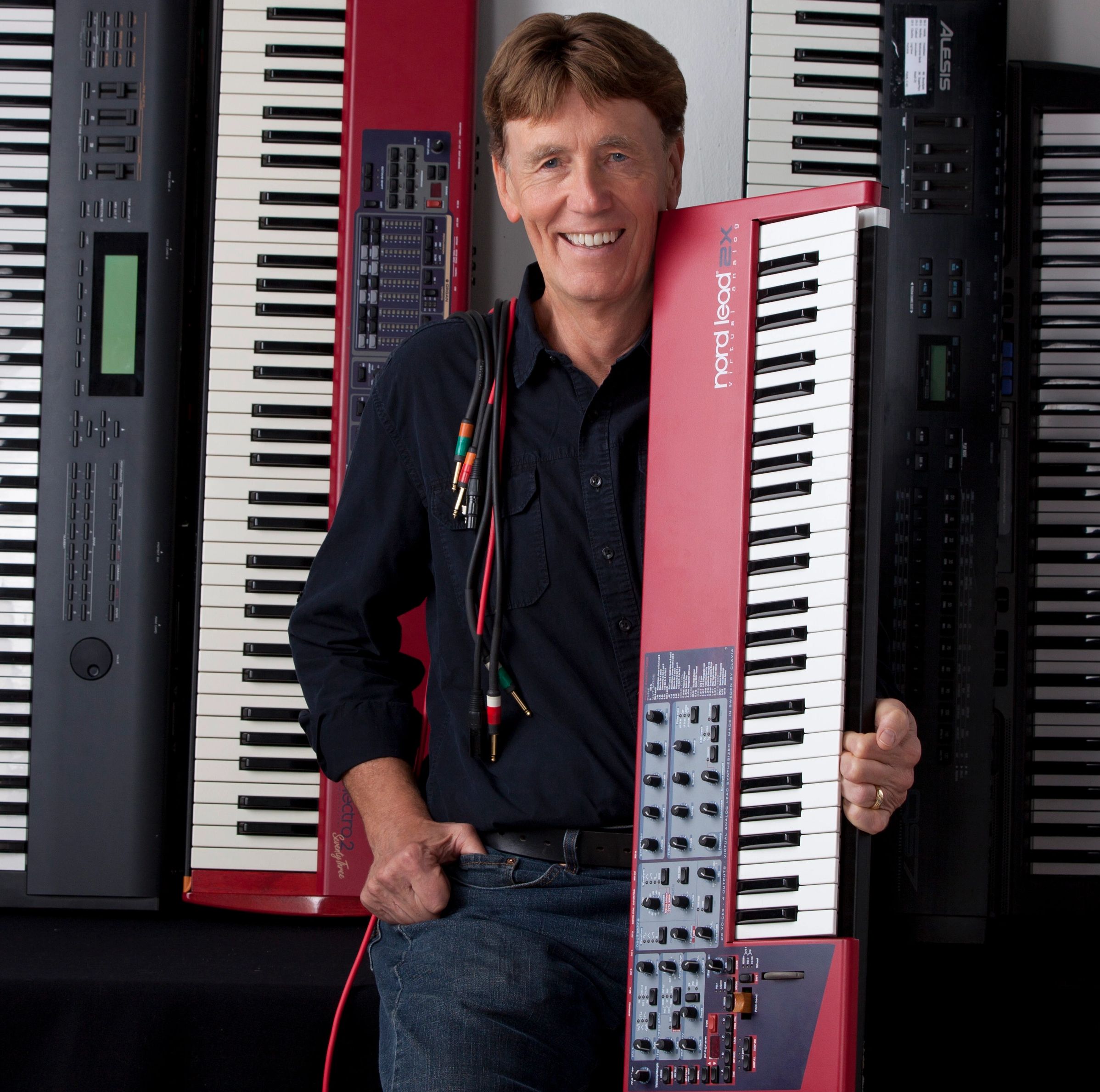 Smiling man holding a red Nord Lead 2X keyboard synthesizer.