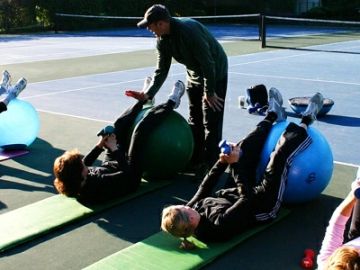 People exercising with fitness balls outdoors under instructor guidance.