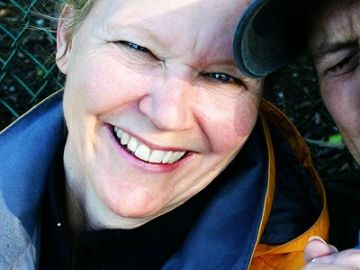 Close-up of a smiling woman outdoors with a partial view of another person.
