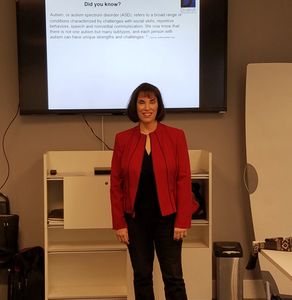 Lori Daly presenting at a seminar with a slide on Autism in the background