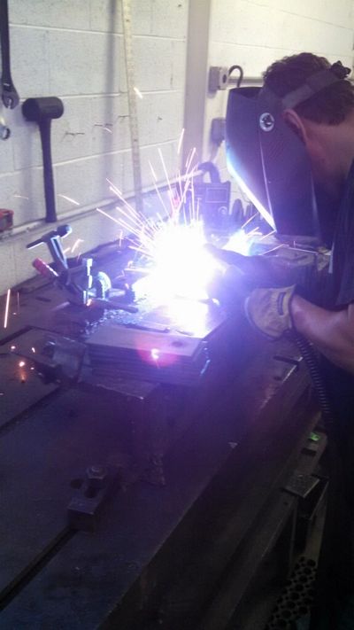 Worker welding metal in a workshop with sparks flying.