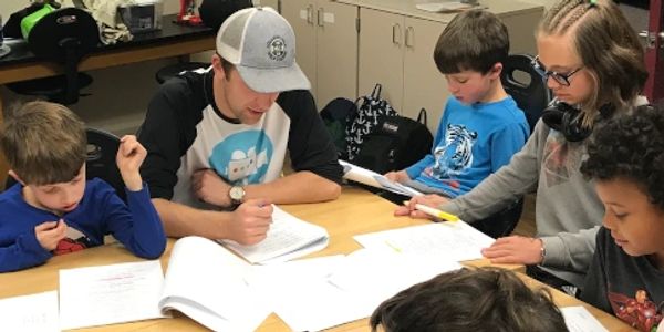 A group of young students and one of our instructors doing a script read at a desk.