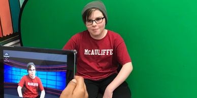 A young student filming in front of a popup green screen. you can see him in an ipad too.
