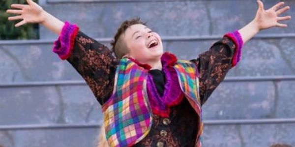 A young musical theater student performing. He's standing up, singing happily, his hands in the air.