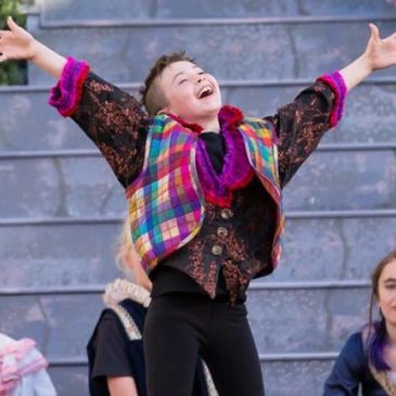 A young musical theater student performing. He's standing up, singing happily, his hands in the air.