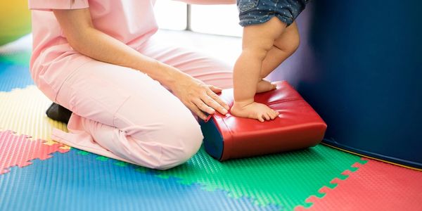 baby legs stepping on a red foam pillow assisted with an adult