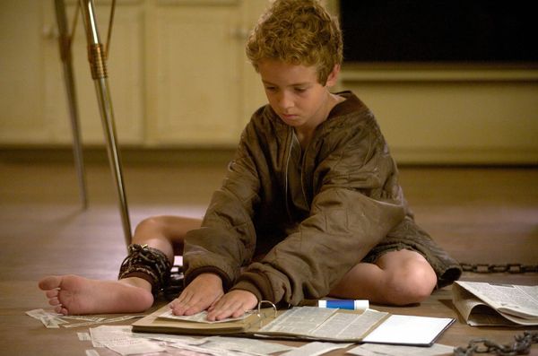 Chained - boy in soiled clothes, chained  on floor and reading a book