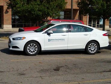 White sedan parked in a lot near a brick building.