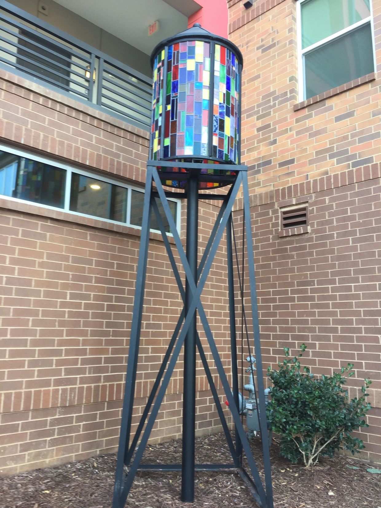 A multicolor stained glass cylinder made to look like a water tower is supported by metal framing