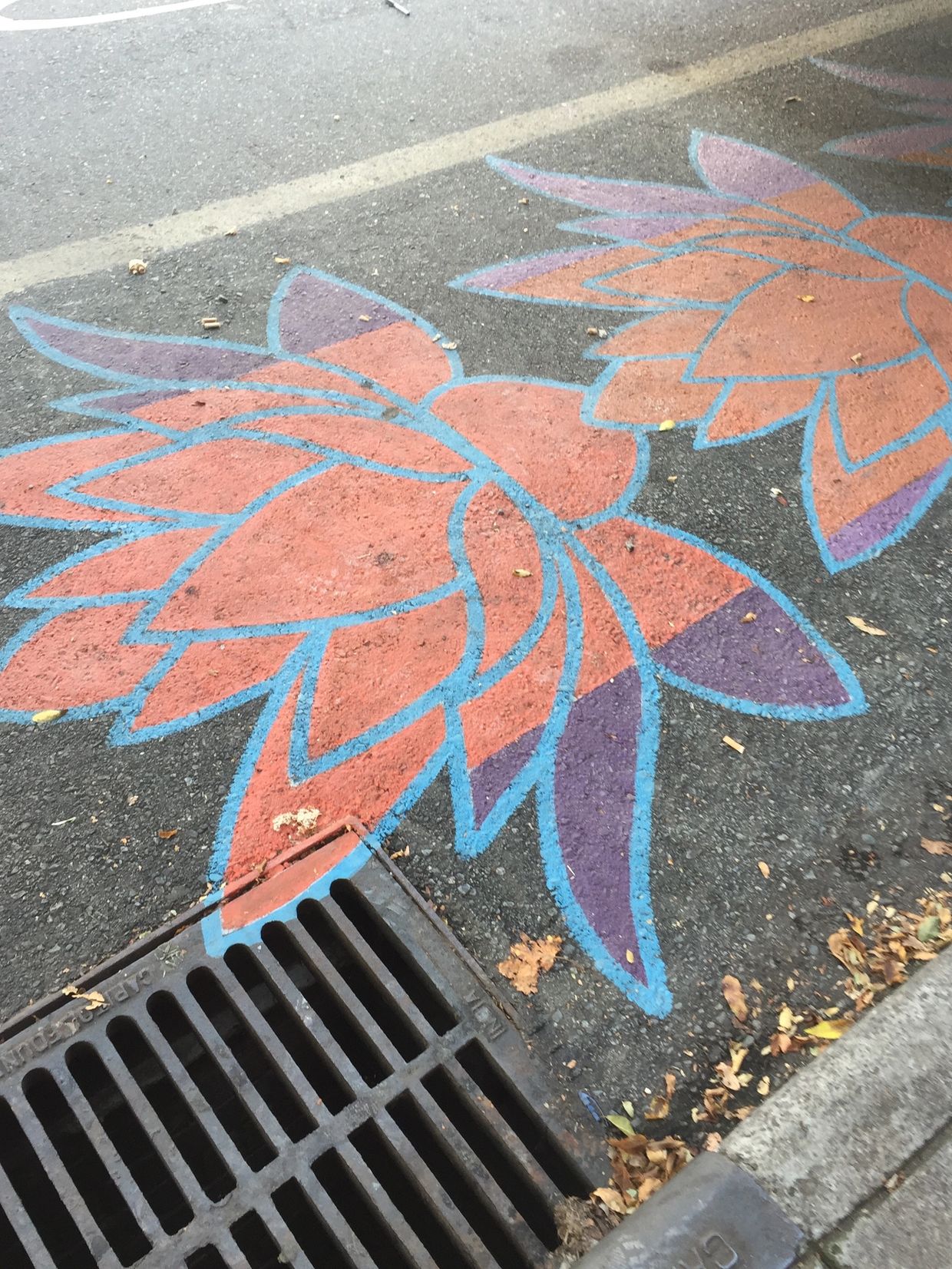 Street mural of a norange lotus flower blossom with a blue outline lining the edge of the street