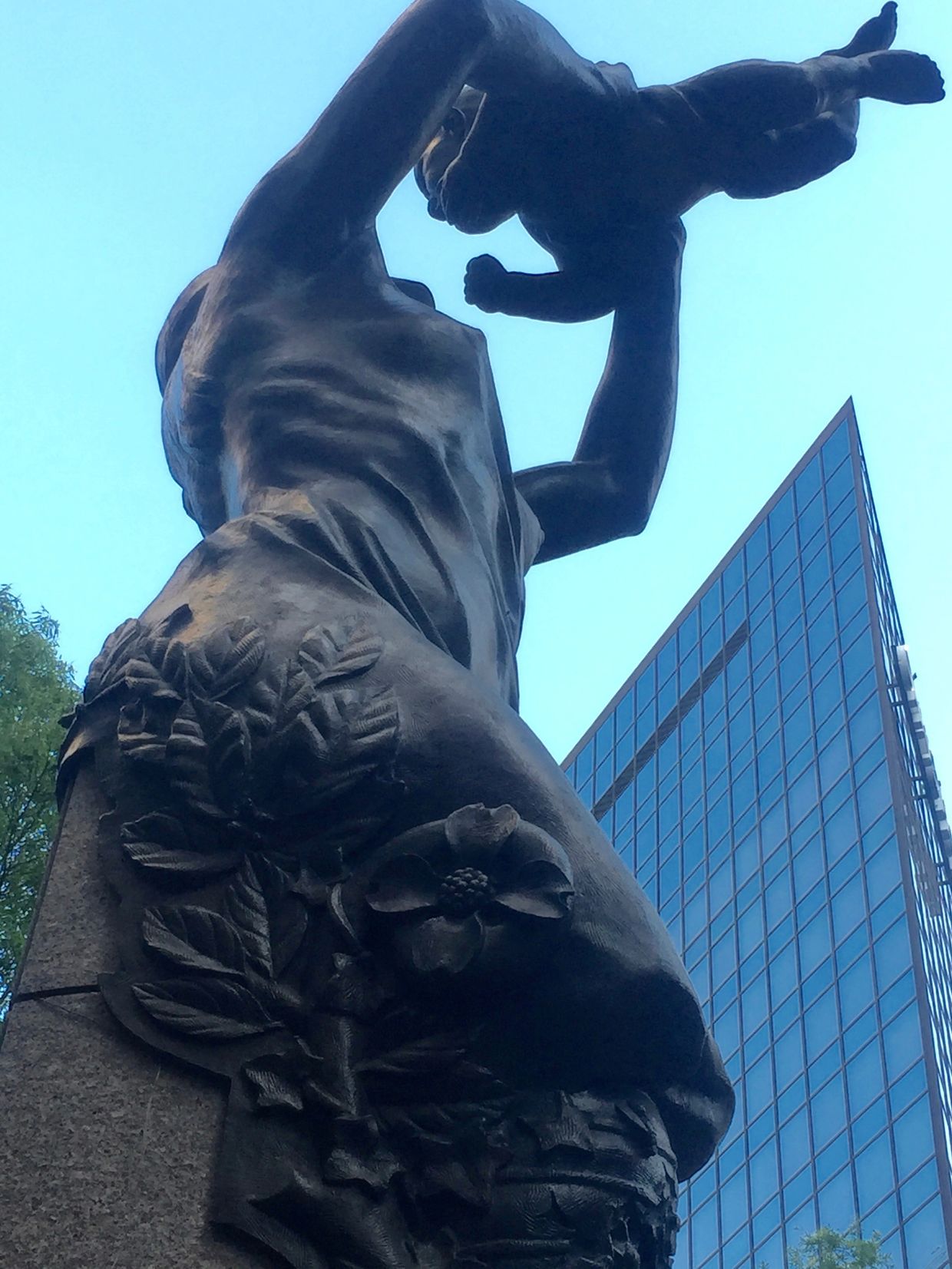 Bronze statue of a mother holding up her child in the air with both hands as they face each other.