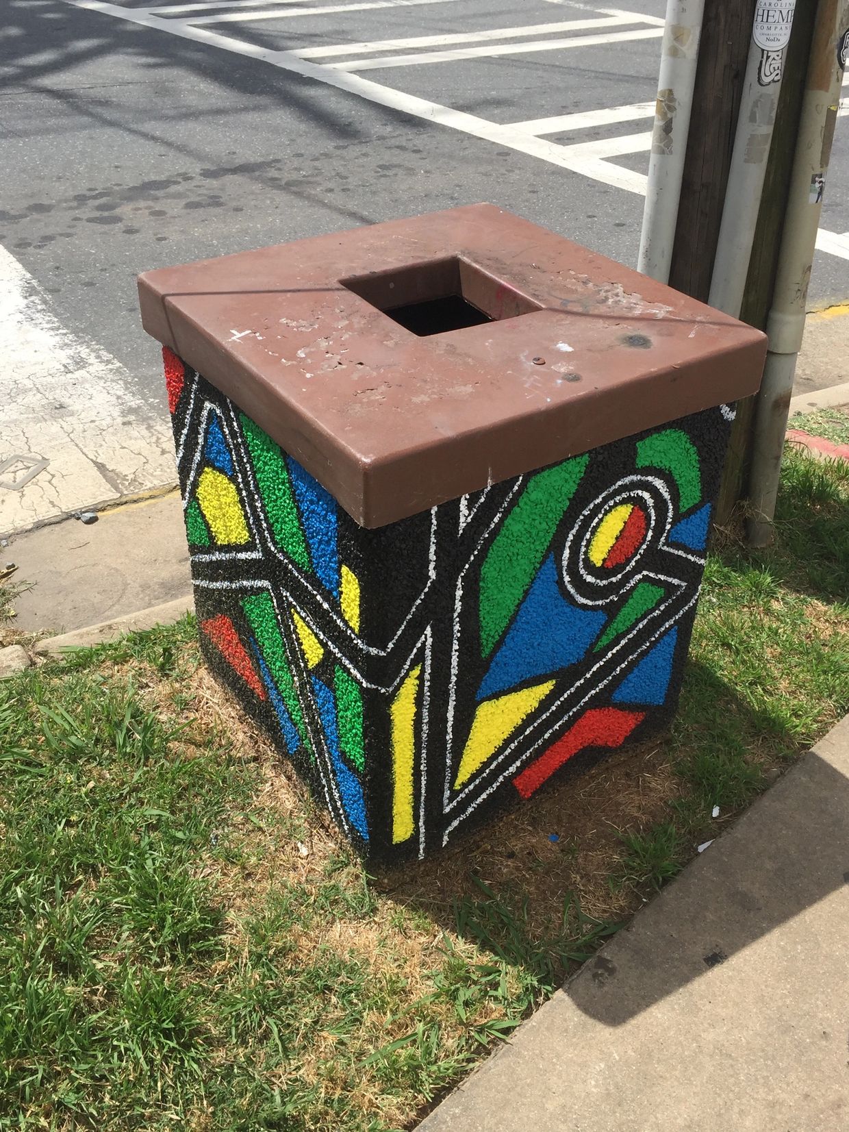 Public trash can with geometric green, red, blue, and yellow shapes and black and white stripes