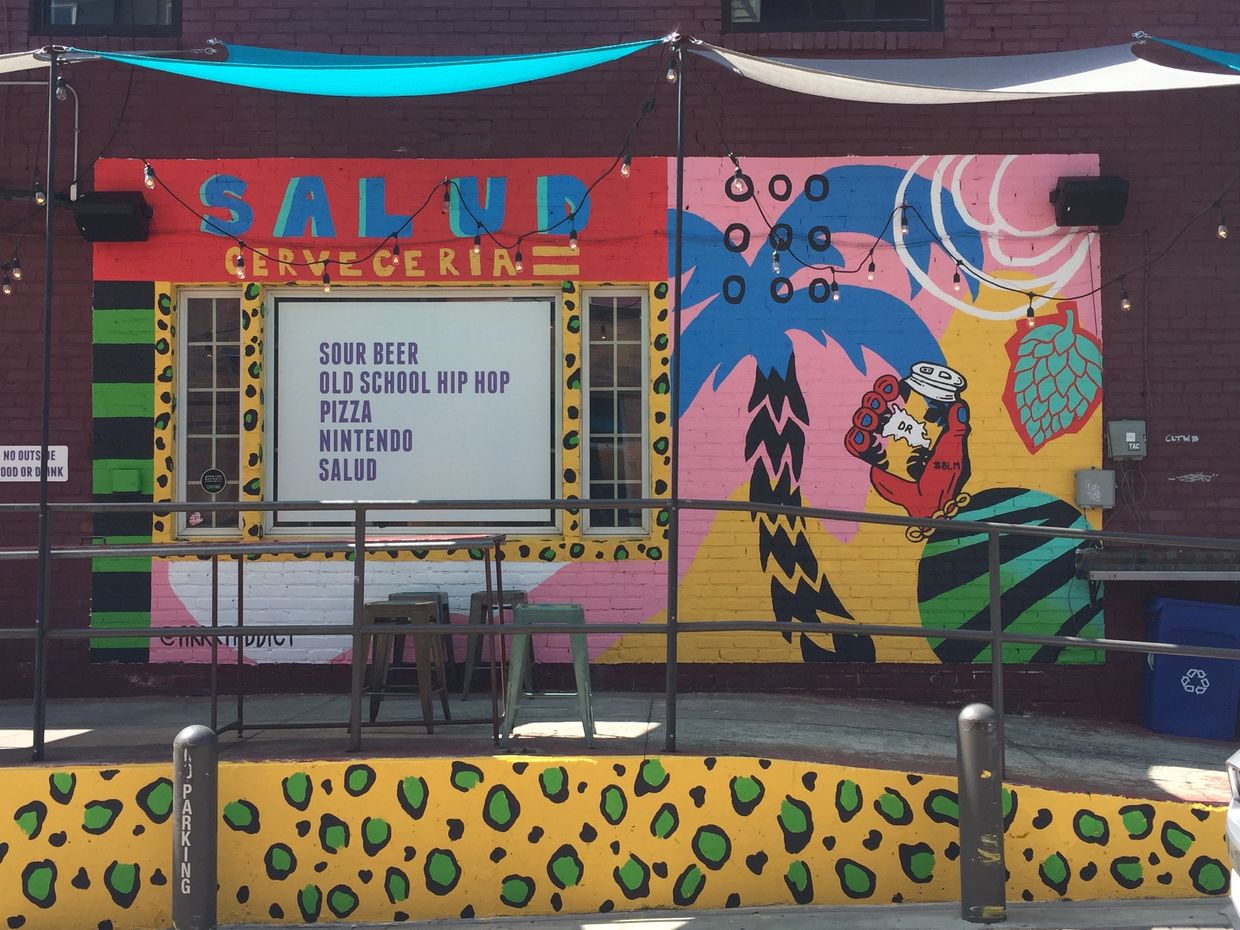 Blue palm tree with hops and a red hand and SALUD written in blue on a red background with patterns
