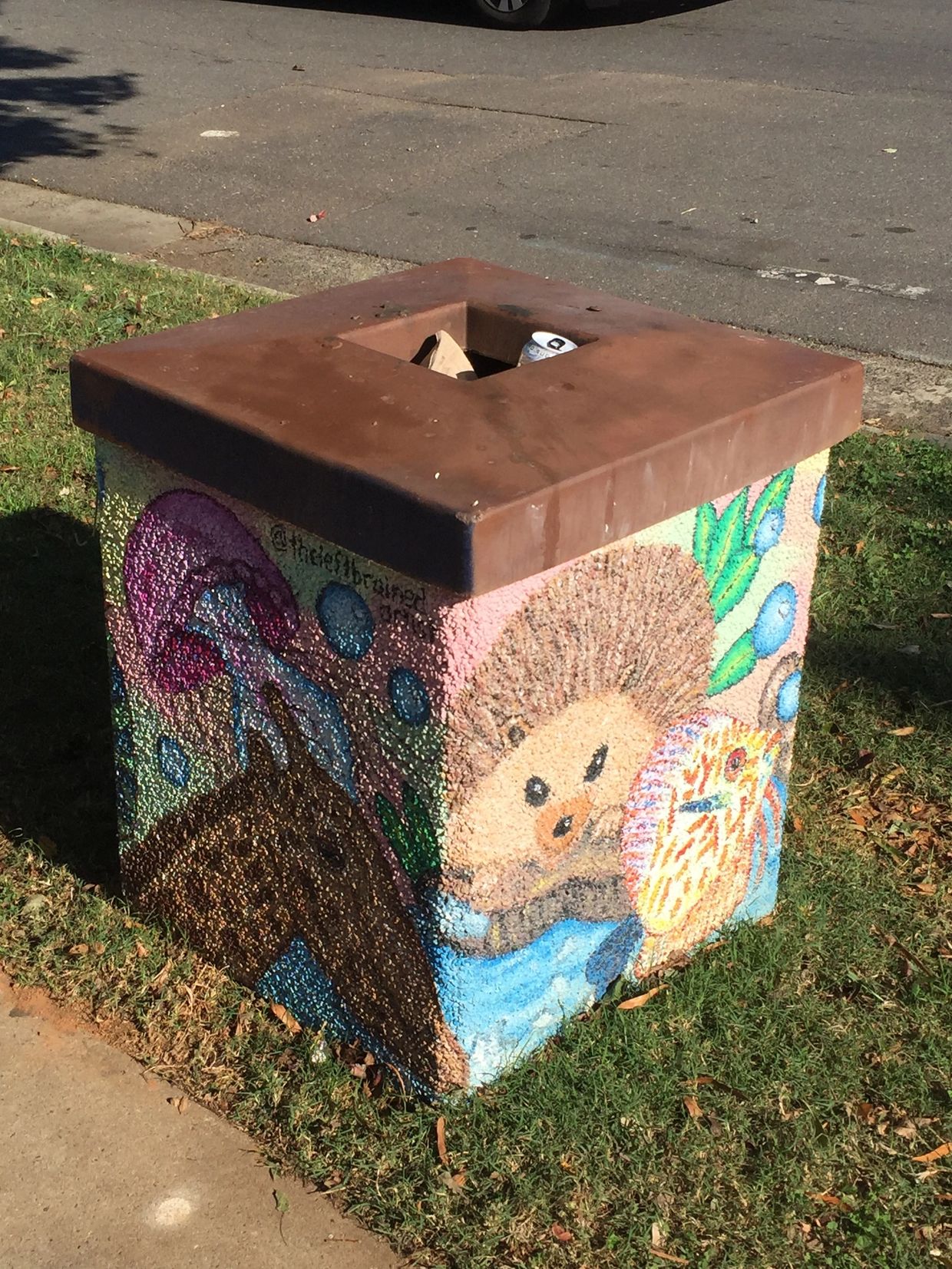 Large public trash can paint with a porcupine and fish and colorful shapes in the background.