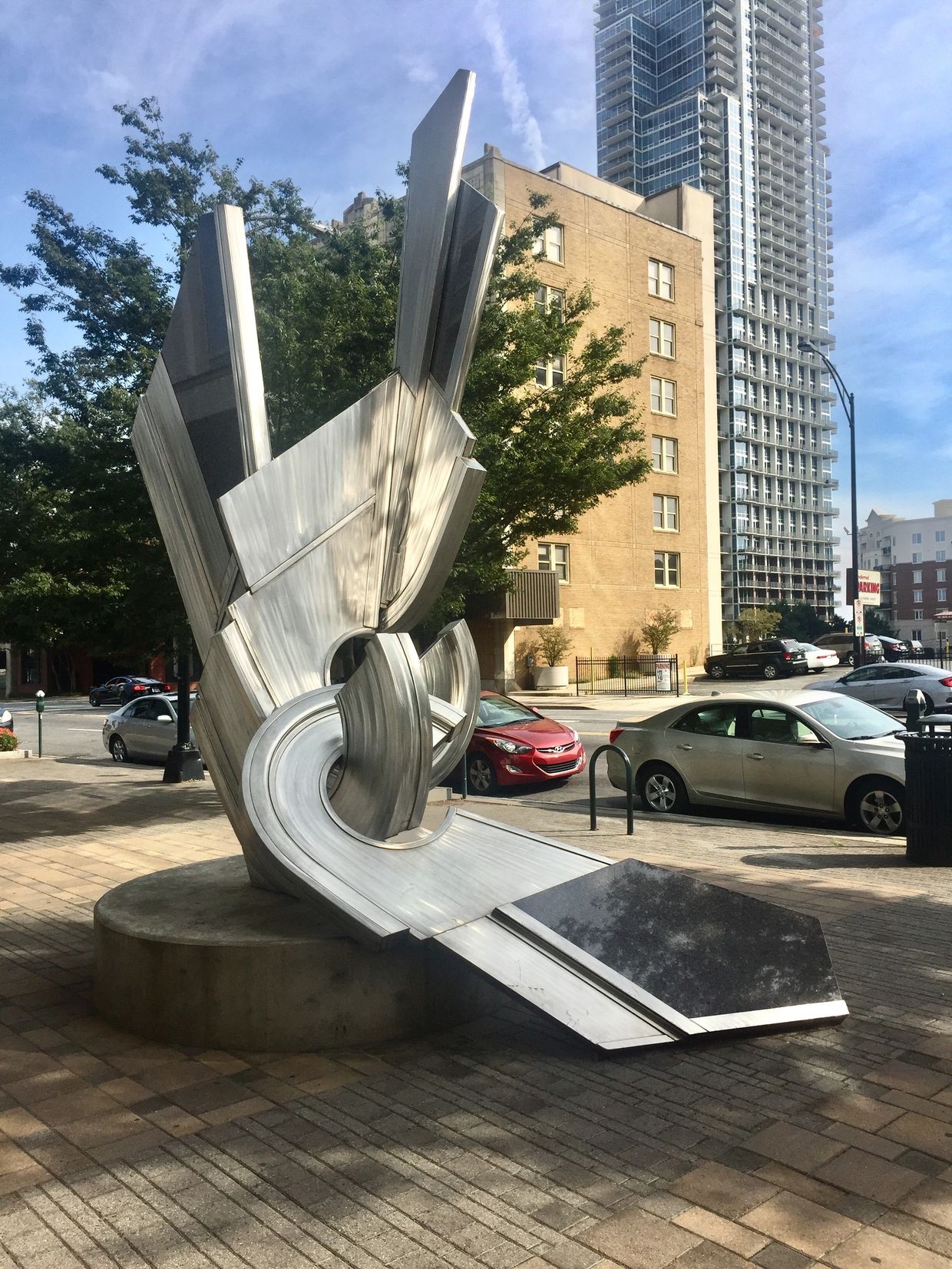 A stainless steel and black granite sculpture with interlocking curves and protruding rays.