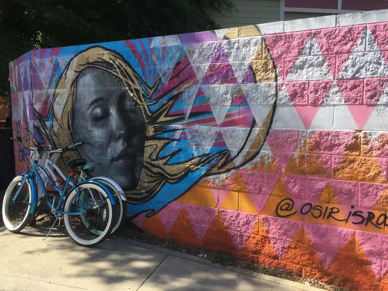Mural on a concrete block fence with a grey-scale human face and orange, pink and white triangles