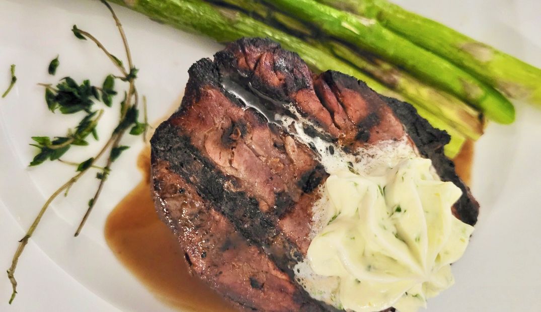 Filet mignon with a rosette of seasoned compound butter, asparagus and fried thyme on a white dinner