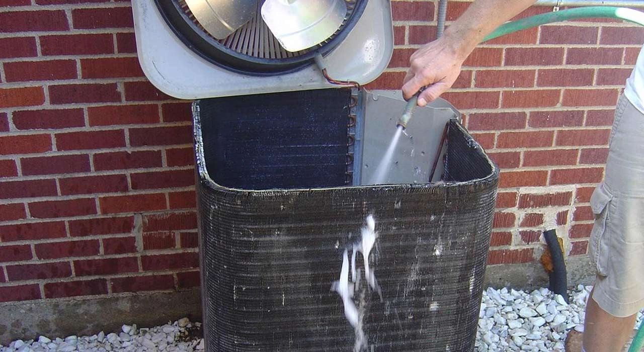 Man washing an AC condenser with a water hose