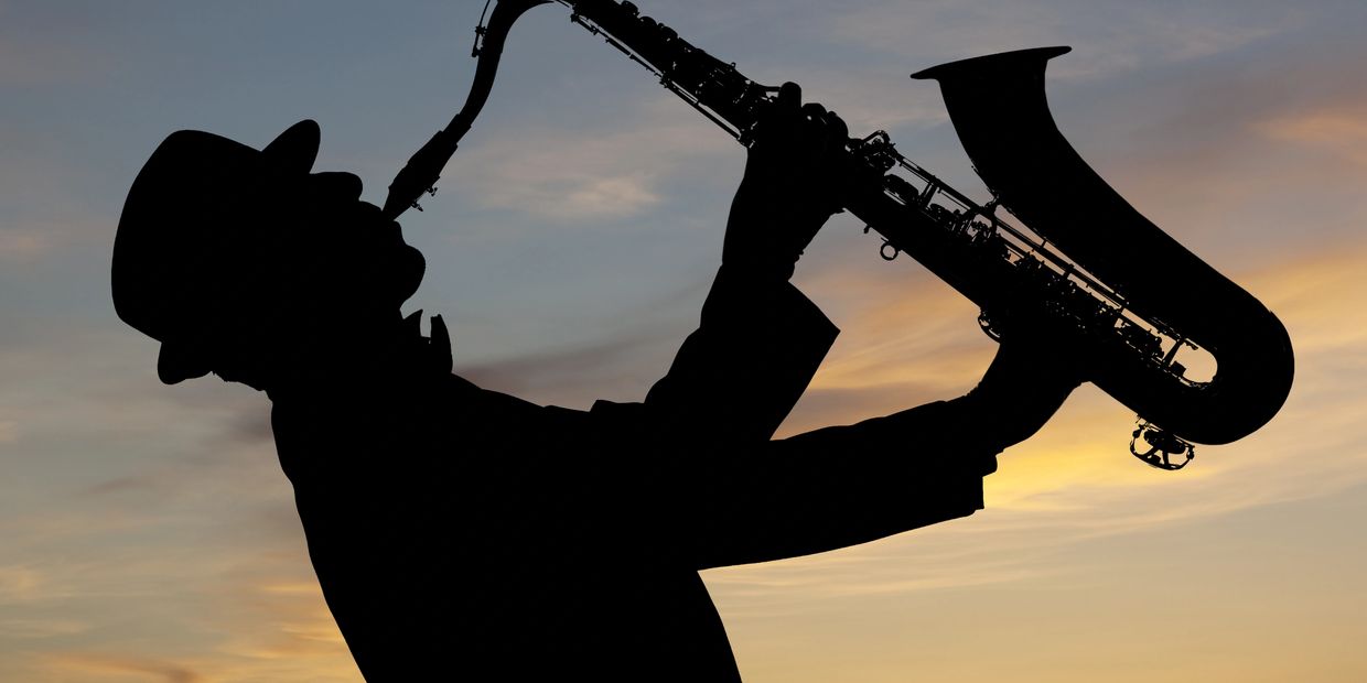 Silhouette of a musician playing saxophone against a sunset sky.