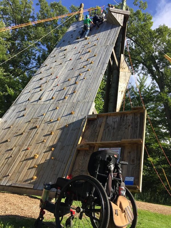 Wheelchair at the bottom of an accessible climbing wall while the owner is completing his climb.