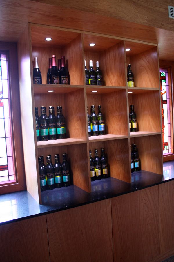 Timber wine display shelves with spot lighting and stained glass windows in cellar door setting.