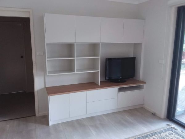 Modern white entertainment unit with timber top, open shelving, and mounted overhead cabinets.