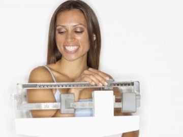 Photo of a woman on a scale weighing herself with a big smile on her face