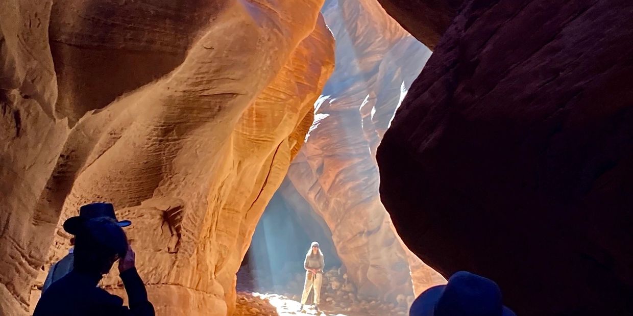 Woman standing in beams of light inside Buckskin Gulch slot canyon as others take her photograph