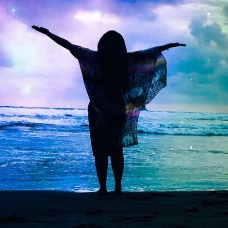 Picture of a woman standing in front of the ocean with her arms wide open. life coach psychic medium