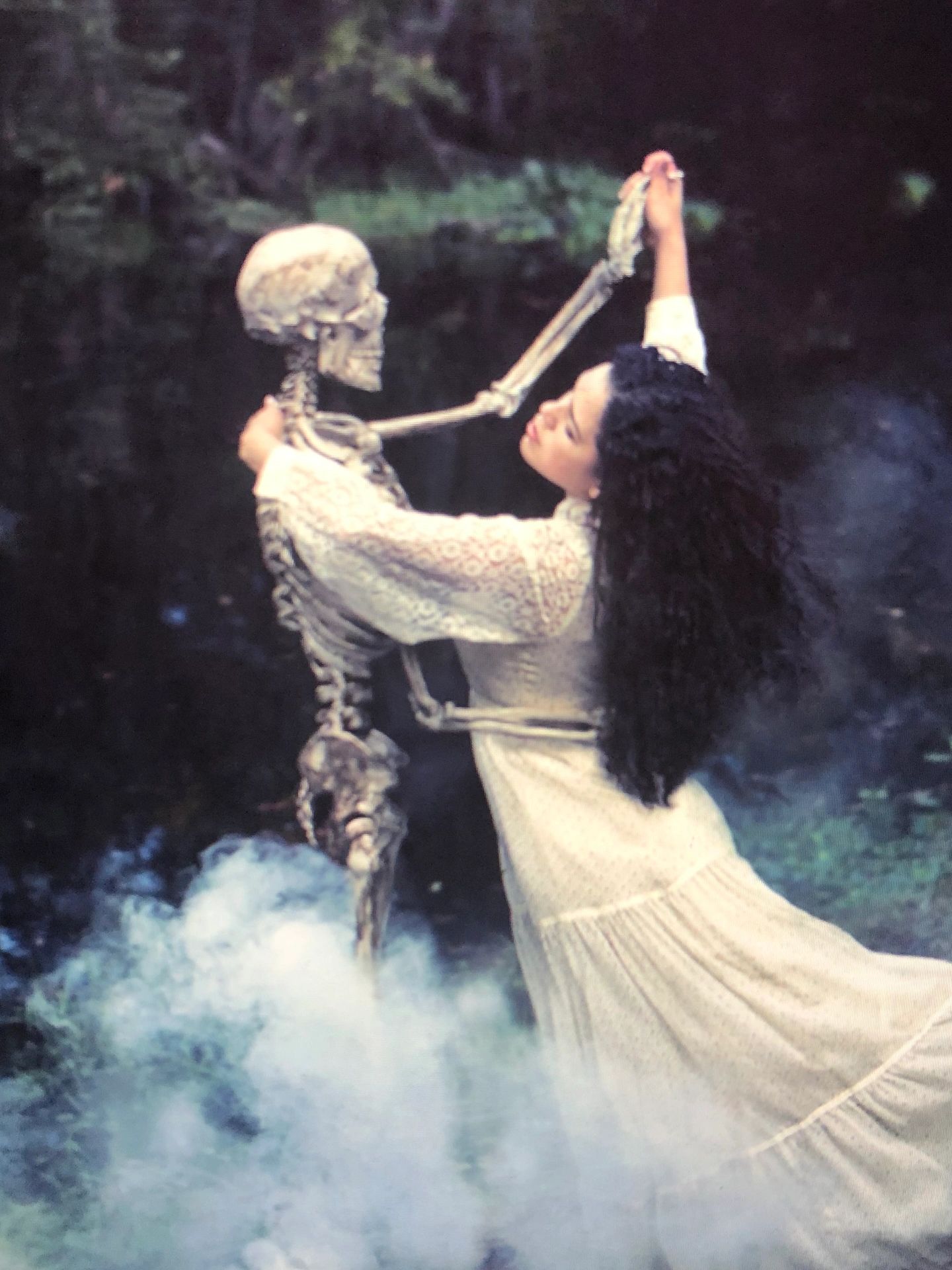 Woman dancing with a skeleton in a misty forest.
