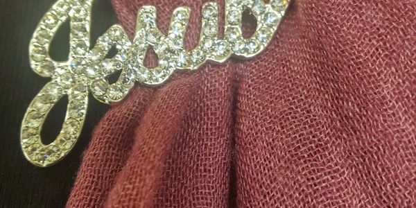 A jeweled name pin on maroon fabric.