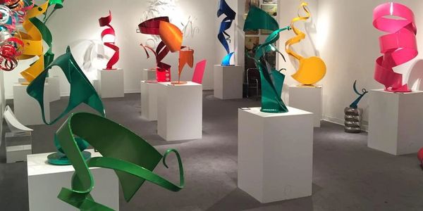 Colorful abstract metal sculptures displayed on white pedestals in a gallery.