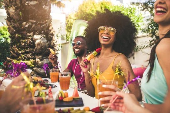 Friends enjoying a sunny outdoor meal with drinks and laughter.