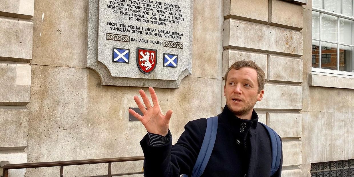 A tour guide speaking next to a commemorative plaque with the flags during private London tours.