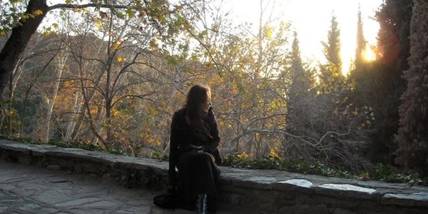 Woman sitting on a rock wall staring at the sunset.