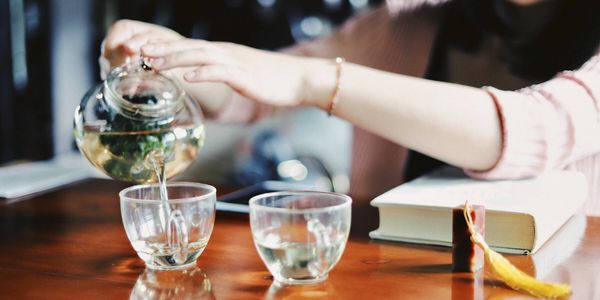lady POURING hot TEA INTO GLASS TEACUPS ON WOOD TABLETOP book on table