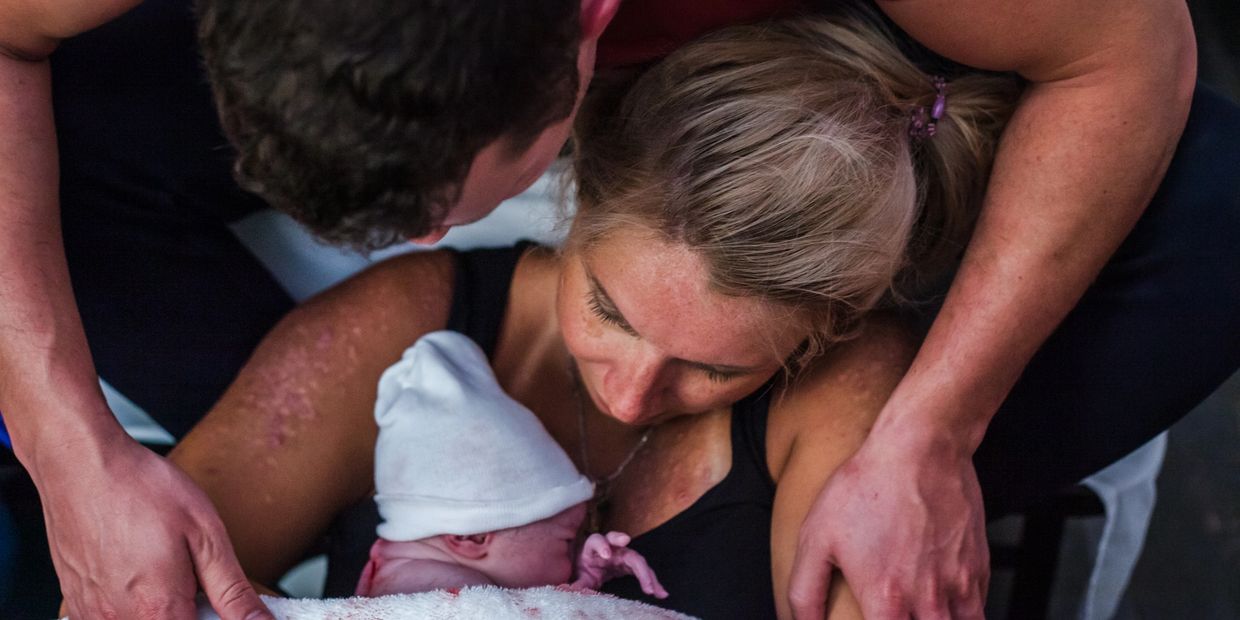 Mother holding newborn baby wrapped in a blanket while dad holds her arms