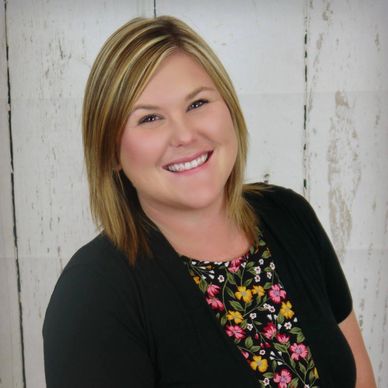 Smiling woman with blonde hair wearing a floral blouse and black cardigan.