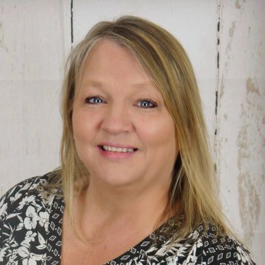 Smiling woman with blonde hair wearing a patterned blouse.