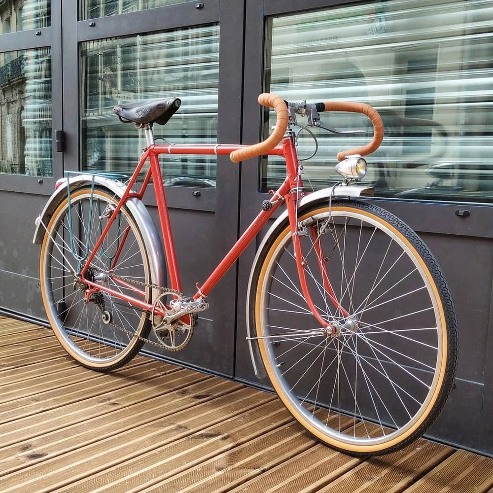 vélo randoneur rouge avec pneu bicolore noir et marron, guidoline marron clair et selle cuir marron 