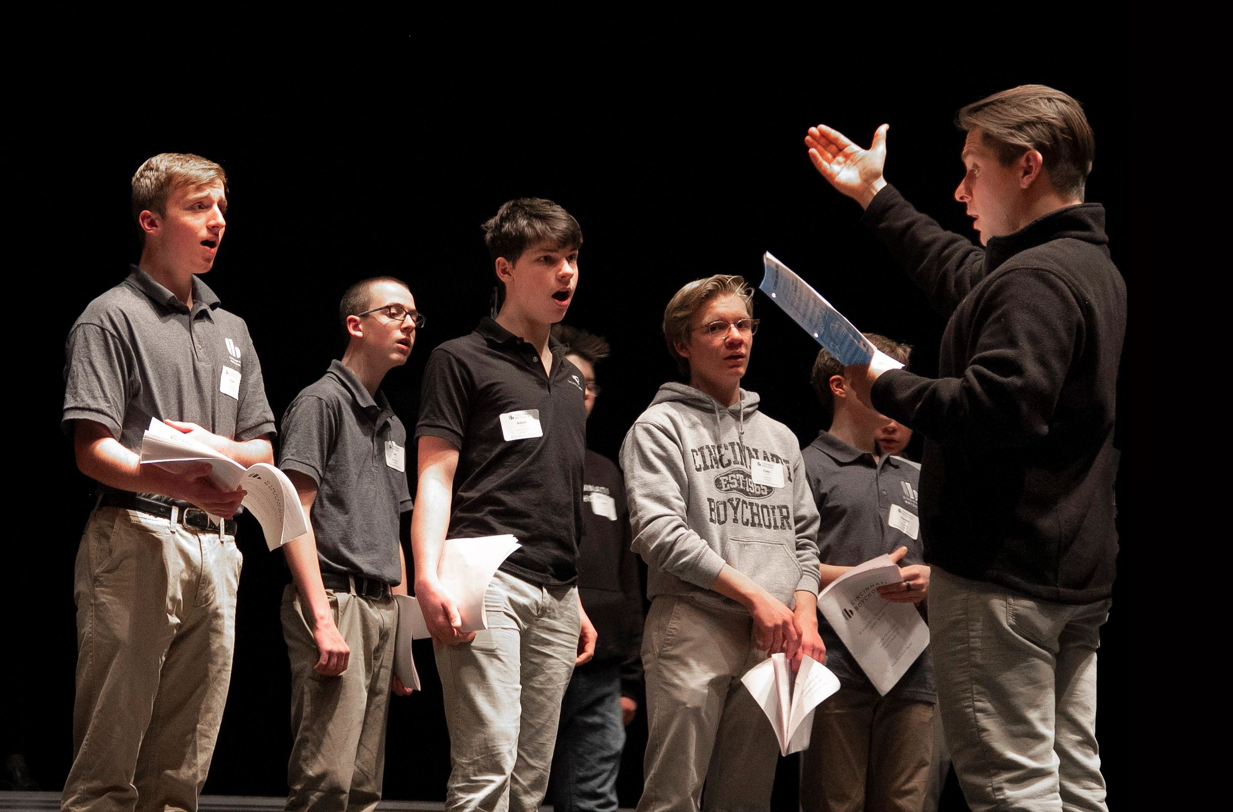 Young men rehearsing with a conductor on stage.
