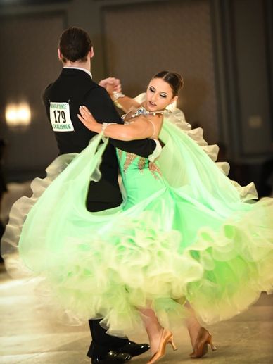 Competition ballroom dancing her dress is green and spinning he is in a suit 