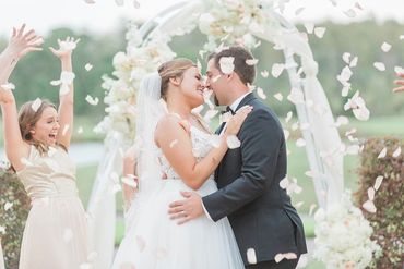 Bride and Groom first kiss under arch and rose petals in the air