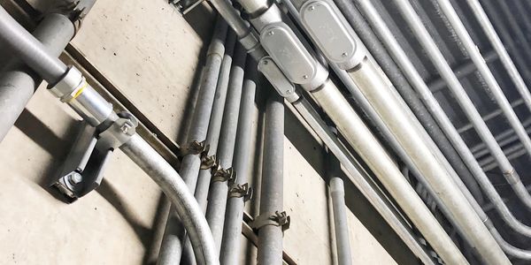 Metal pipes and conduits against a concrete wall.