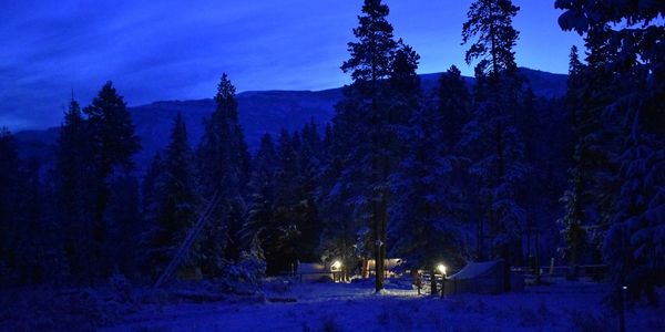 Snowy wall tents and the cozy light of lanterns in Elk Fork Outfitters' Wilderness Camp