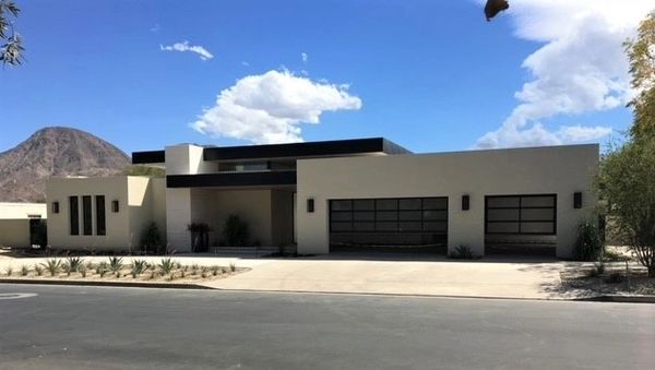 Modern single-story house with flat roof and desert landscaping under blue sky.