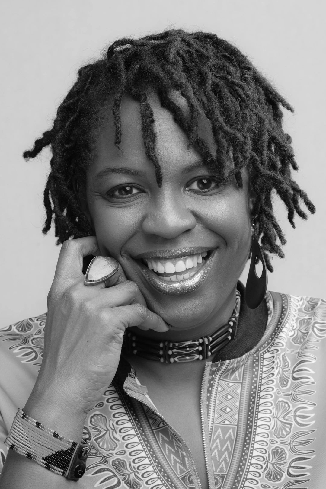 Smiling woman with dreadlocks and patterned clothing.