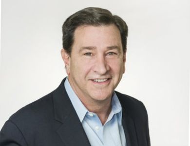 Professional man in business attire smiling against a plain background.