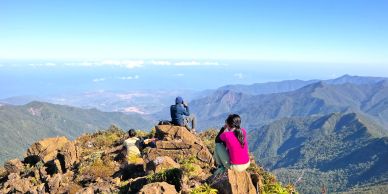 People enjoying panoramic mountain views from a rocky summit on a clear day.
