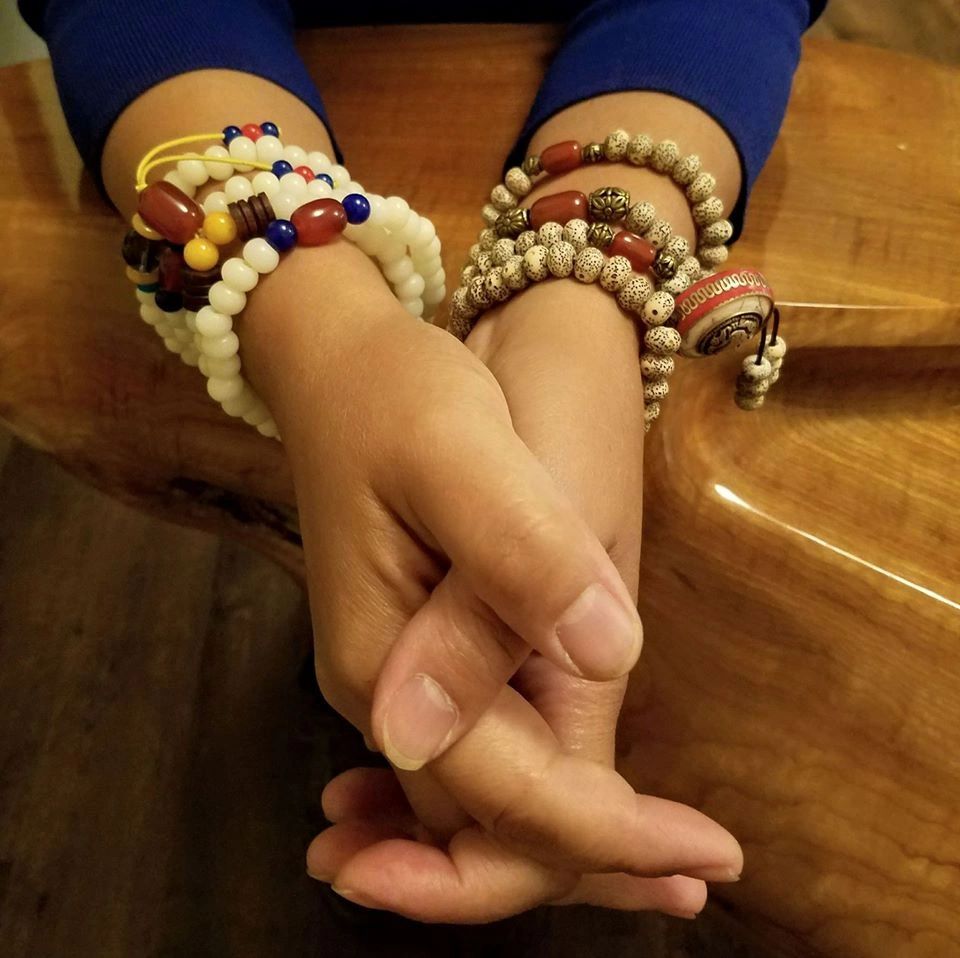 A woman's clasped hands with both wrists adorned with Buddhist mala beads. 